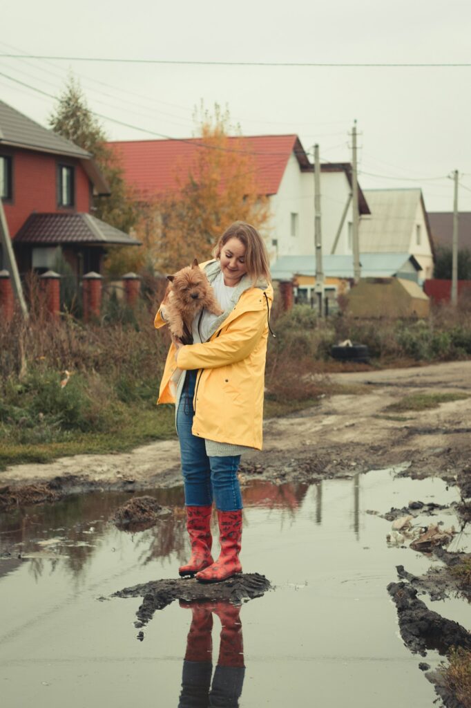 a girl in a yellow raincoat with a dog in her arms is standing in the middle of a puddle