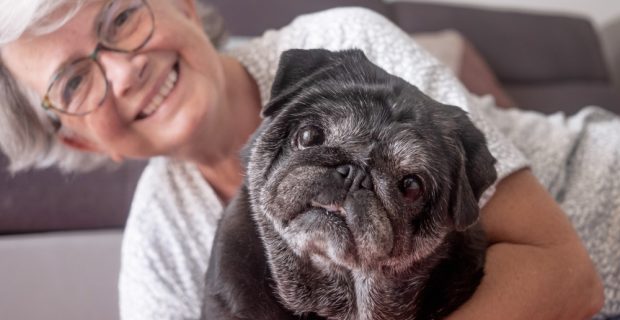 mulher de cabelos brancos abrançando um Pug de pelos pretos e bracos