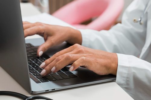 mãos de uma mulher com jaleco digitando em um notebook