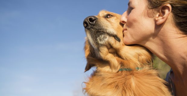 A woman kissing a pet dog on the cheek.