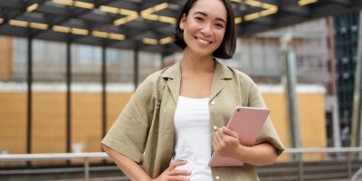 City girl standing with tablet on street, using application, smiling at camera