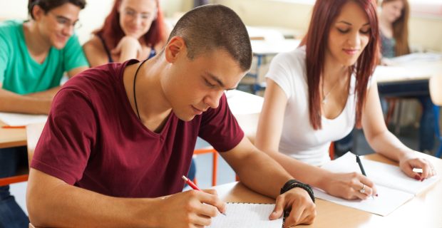 Portrait of high school student at desk during the class. Students are writing in their notebook.