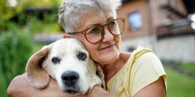 Portrait of senior woman sitting outdoors in garden, holding pet dog.