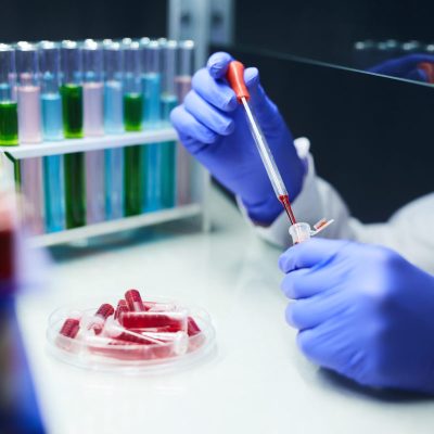 Close up of unrecognizable scientist dropping blood samples in test tubes while working on research in laboratory, copy space