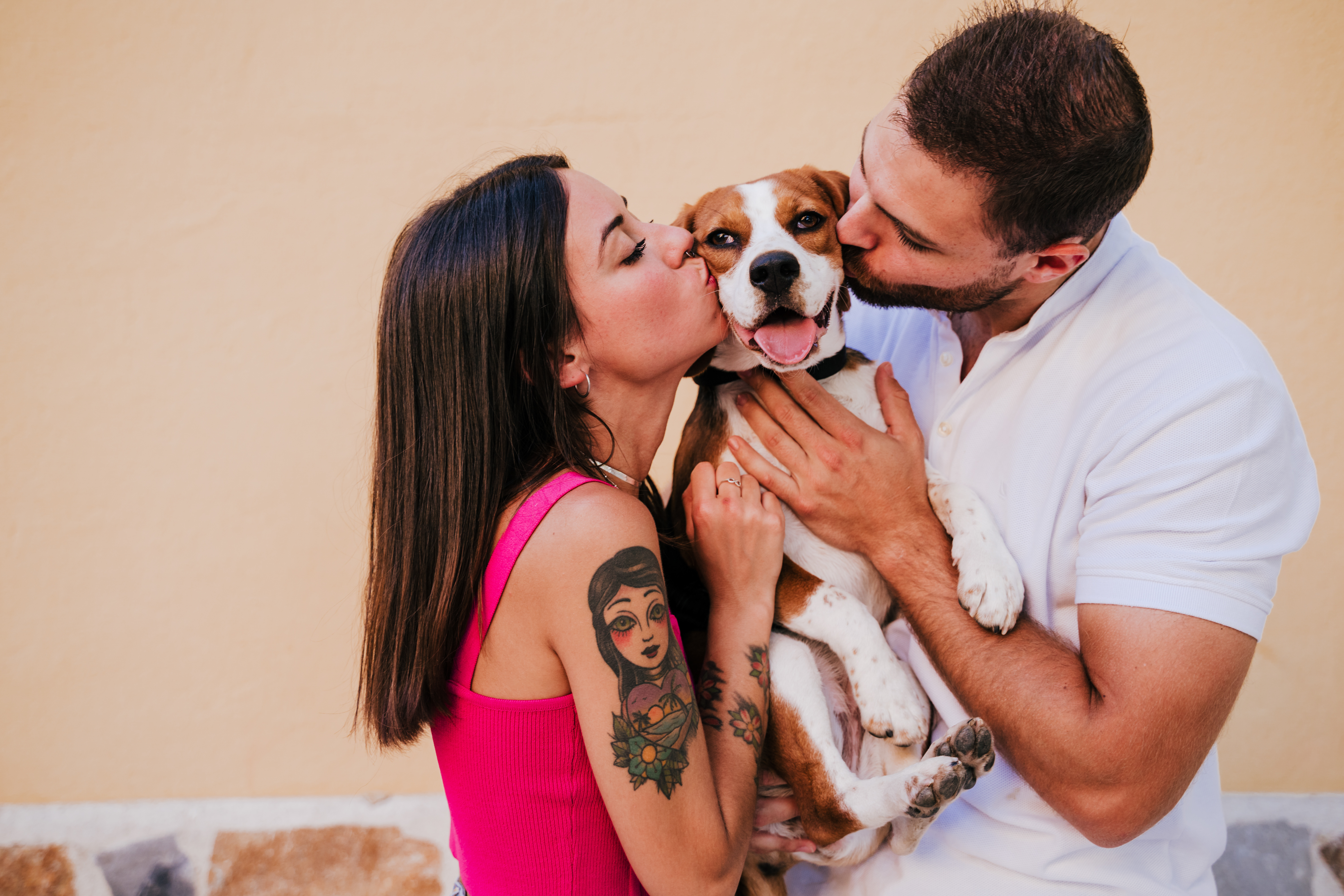 happy young couple outdoors kissing their beagle dog. Family and lifestyle