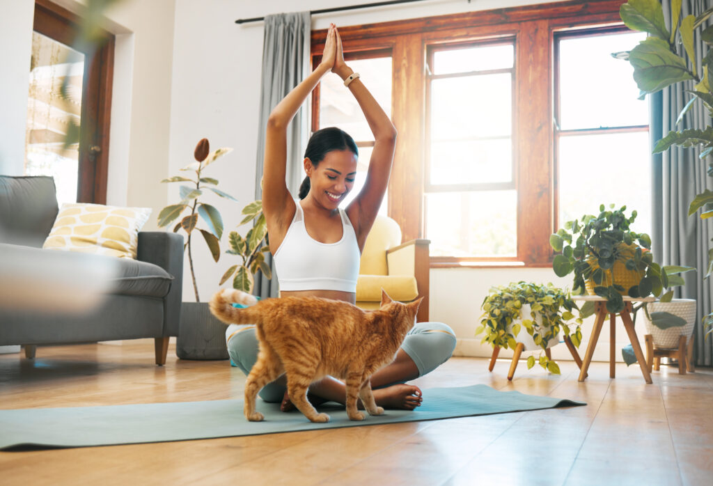 Shot of a sporty young woman meditating at home with her pet cat